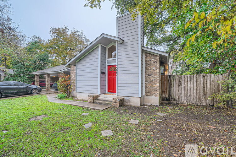 A house with a red door is surrounded by a wooden fence and greenery.