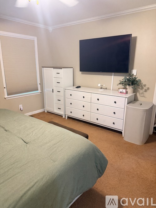 A bedroom with a bed, dresser, and a television mounted on the wall.