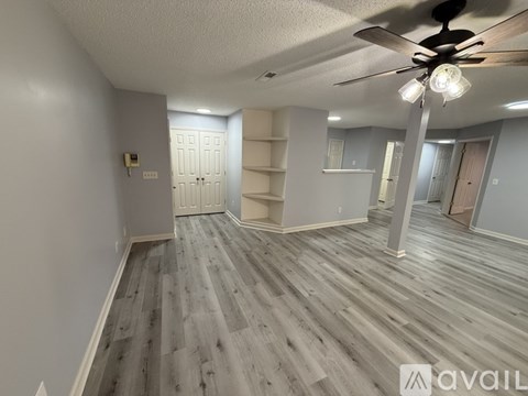 A spacious room with a ceiling fan and light fixture, featuring wood flooring and a white door.