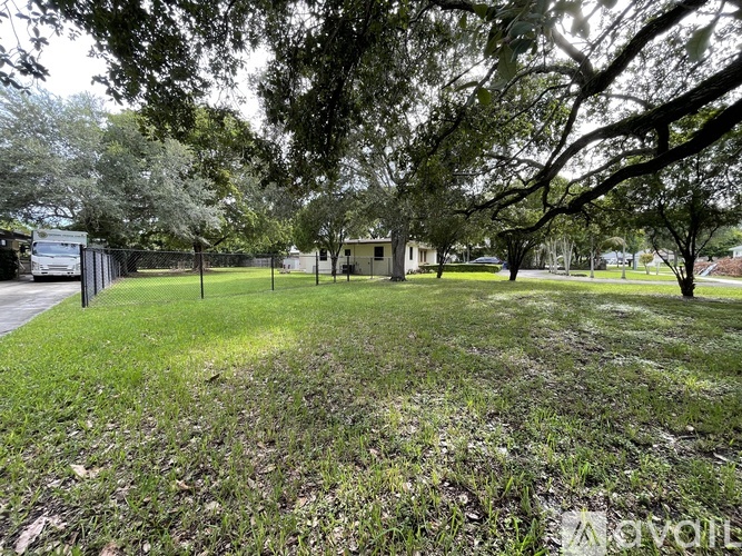 A grassy area with trees and a fence in the background.