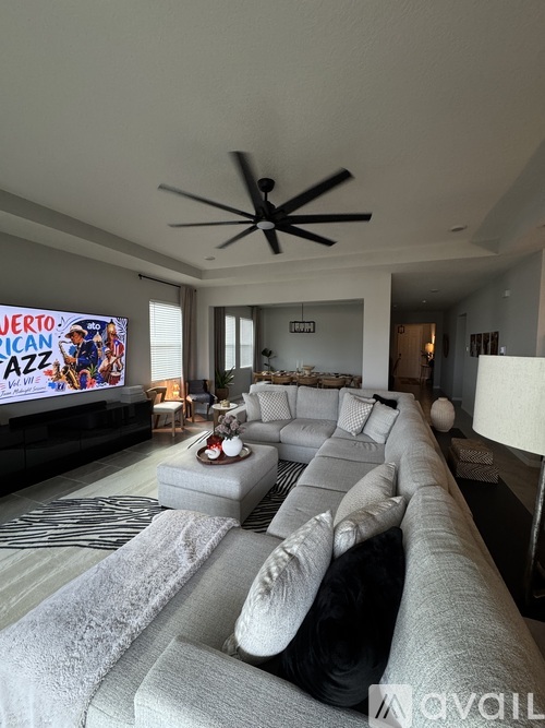 A living room with a large grey sofa and a ceiling fan.