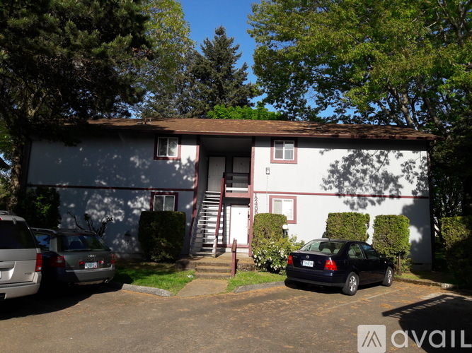 A house with a white and red exterior is surrounded by trees and has a car parked in front.