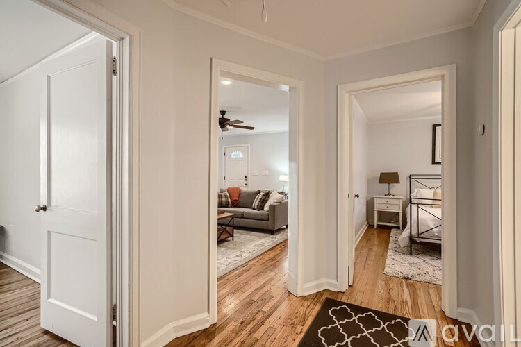 A bedroom with a bed, nightstand, and lamp is visible through an open door.