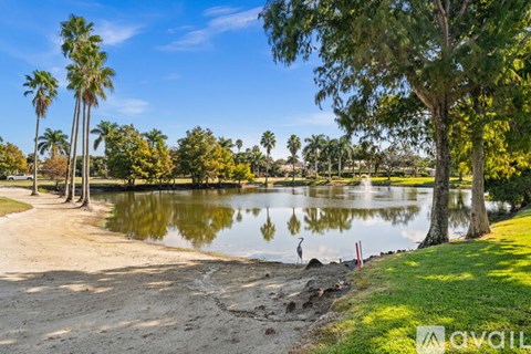 A serene park with a lake, palm trees, and a clear blue sky.