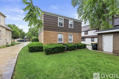 A house with a brown and grey exterior is surrounded by a green lawn and a sidewalk.