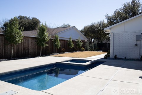 A swimming pool in a backyard with a white house and a wooden fence.
