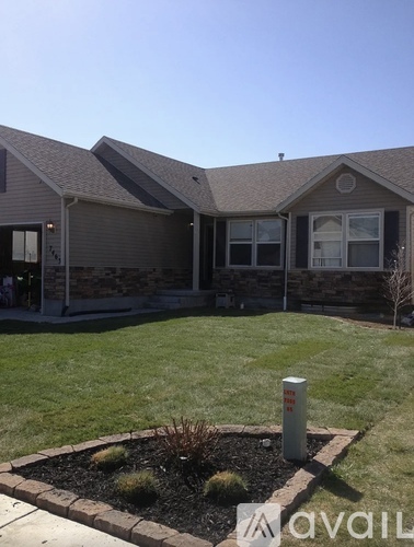 A house with a brown roof and a grey wall with a small garden in front.