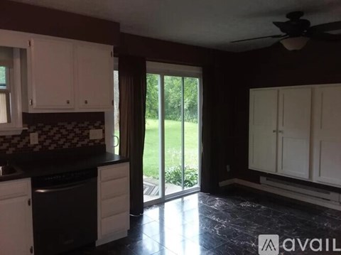 A kitchen with white cabinets and a black countertop with a dishwasher and a window.