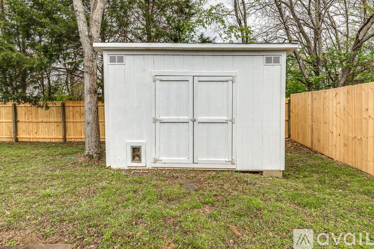 A small white shed with a door and a window is situated in a grassy area.