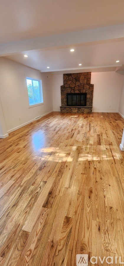 A spacious room with wooden flooring and a stone fireplace.