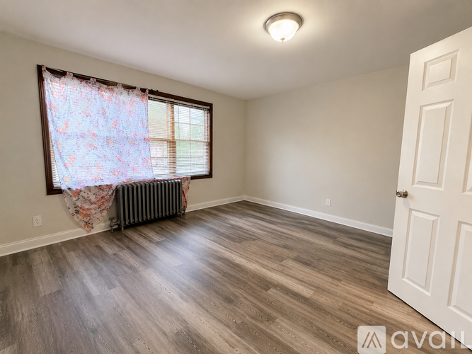 A room with a window covered by a floral curtain and a radiator beneath it.