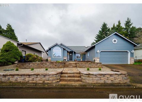 A house with a blue garage door is surrounded by a stone wall and steps leading to the front door.