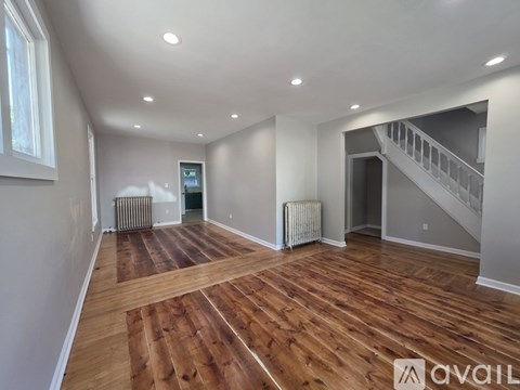 A spacious room with wooden floors and a staircase in the background.