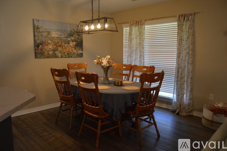 A dining room with a table set for six and a painting hanging above it.