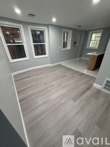A room with grey flooring and white walls, with a window on the left and a fire extinguisher on the right.