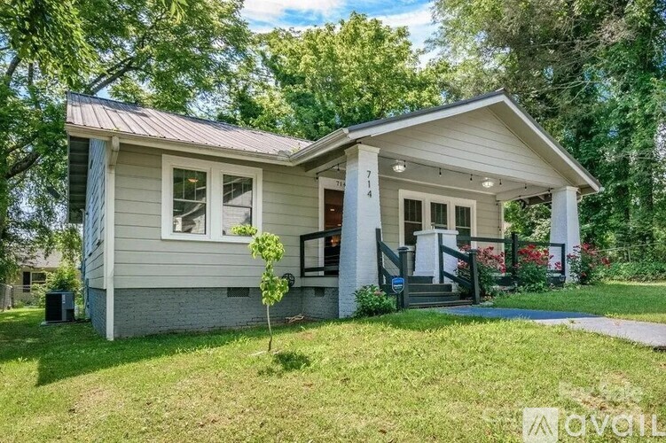 A small house with a porch and a tree in front.