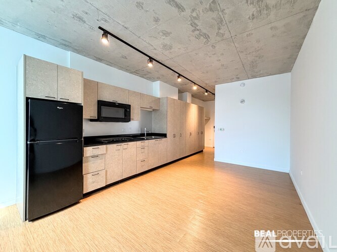 A kitchen with a black fridge and microwave, wooden floors, and a white wall.