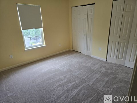 A room with a carpeted floor and a window with a view of trees and a house.