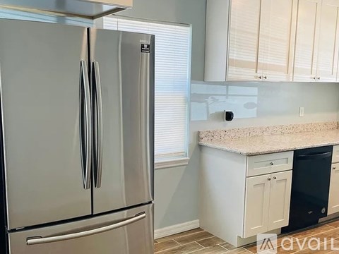 A stainless steel refrigerator stands in a kitchen with white cabinets.