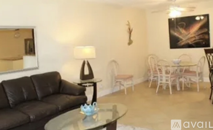A living room with a black leather couch and a glass table with a blue vase on it.