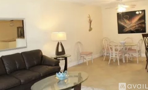 A living room with a black leather couch and a glass table with a blue vase on it.
