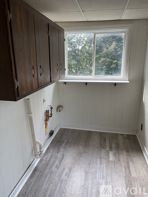 A room with wooden cabinets and a window showing trees outside.