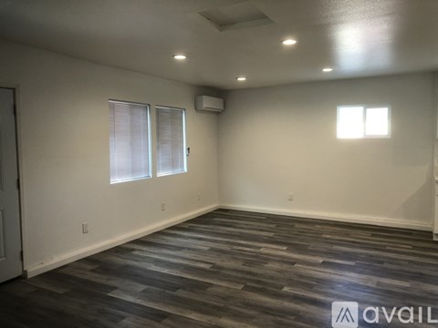 A spacious room with wooden flooring and two windows.