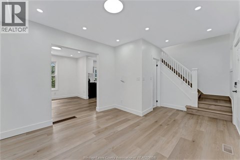 A spacious room with wooden flooring and a staircase leading to another room.