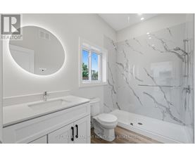 A white bathroom with a marble shower and a round mirror.
