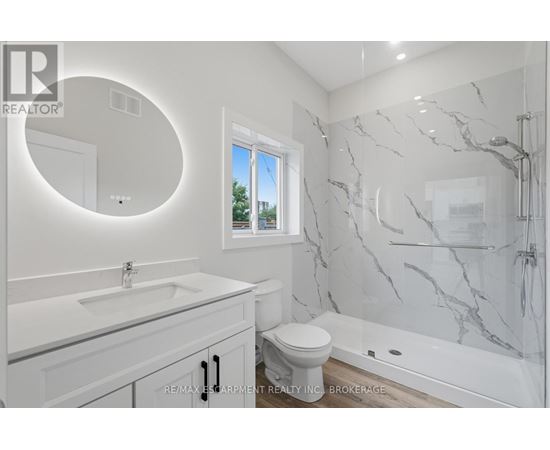 A white bathroom with a marble shower and a round mirror.