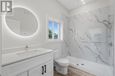 A white bathroom with a marble shower and a round mirror.