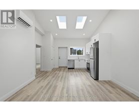 A spacious, empty room with a kitchen area in the background.