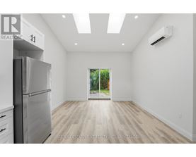 A spacious, empty room with a refrigerator on the left and a window on the right.