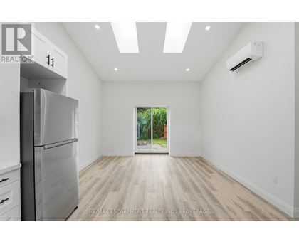 A spacious, empty room with a refrigerator on the left and a window on the right.