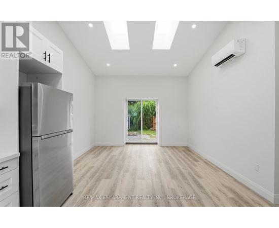 A spacious, empty room with a refrigerator on the left and a window on the right.