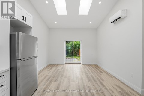 A spacious, empty room with a refrigerator on the left and a window on the right.