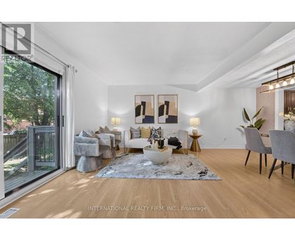 A well-lit, spacious living room with a grey rug, a grey sofa, a white armchair, a grey chair, a wooden floor, a glass door, a table with a vase, a potted plant,