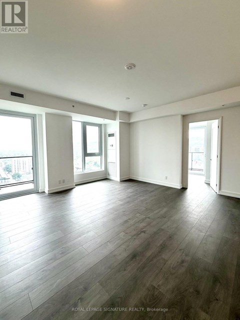 A spacious room with wooden flooring and large windows.
