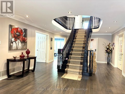 A spacious foyer with a staircase and a painting of red flowers on the wall.