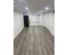 A spacious room with a black fridge and wooden flooring.