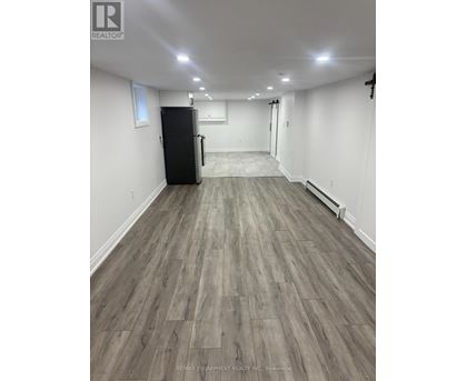A spacious room with a black fridge and wooden flooring.