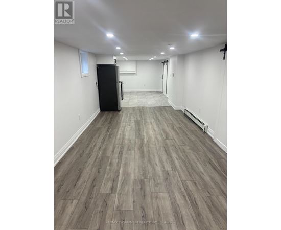 A spacious room with a black fridge and wooden flooring.