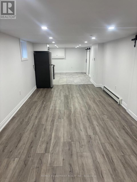 A spacious room with a black fridge and wooden flooring.