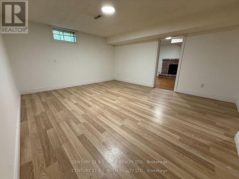 A spacious room with wooden flooring and a fireplace in the corner.