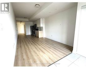 A spacious living room with wood flooring and a kitchen area in the background.