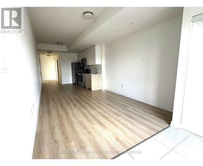 A spacious living room with wood flooring and a kitchen area in the background.