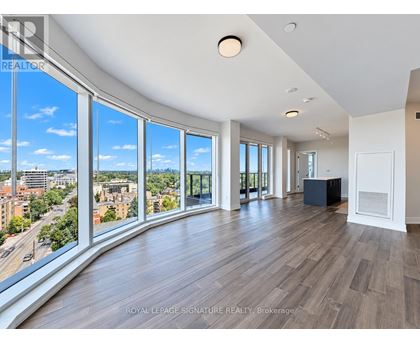 A spacious room with wooden floors and large windows overlooking a cityscape.