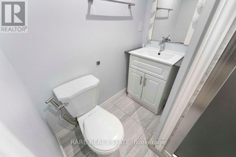 A white toilet is in a small bathroom with a white sink and cabinet.