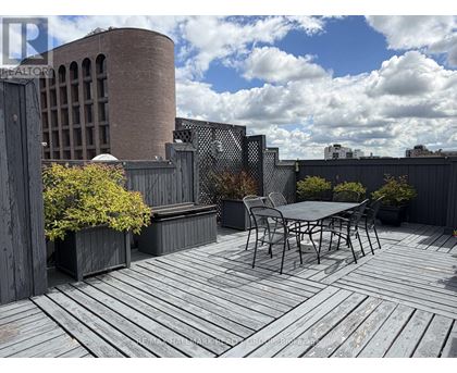 A wooden deck with a table and chairs in the foreground and a building in the background.