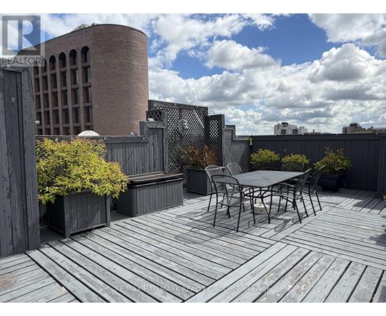 A wooden deck with a table and chairs in the foreground and a building in the background.